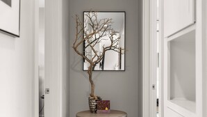 A hallway with a bare tree in a vase, a framed picture on the wall, and a small table with books.