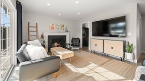 A modern living room with a fireplace, sofa, TV, and a large window.