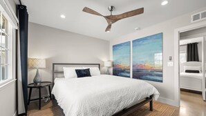 A modern bedroom with a large bed, a ceiling fan, and two large paintings on the wall.
