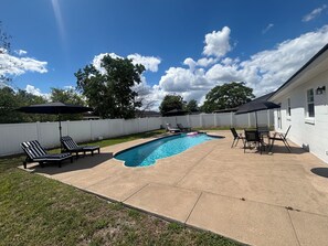 Un jardin avec une piscine, des chaises longues et des parasols.