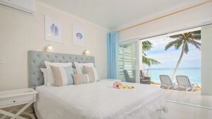 Un dormitorio con una cama grande, una mesita de noche y vista a la playa a través de un ventanal corredero.