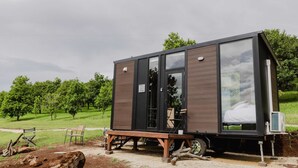Una cabaña moderna y compacta con un amplio ventanal, una pequeña terraza y vistas a un paisaje verde.