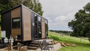 A modern, compact cabin with a wooden exterior, large windows, and a patio area with outdoor seating.