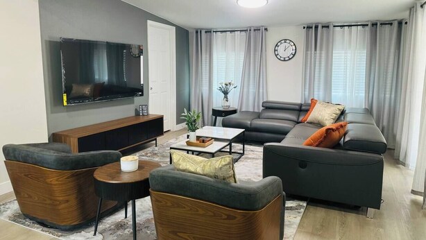 Ein modernes Wohnzimmer mit Flachbildfernseher, einer Sofagarnitur, einem Couchtisch und einem Holz-Akzentstuhl.