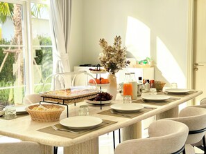 A breakfast setting with a buffet, plates, cutlery, and a vase of flowers. - Mira Maya Villa Nakornnayok (Nakhon Nayok)