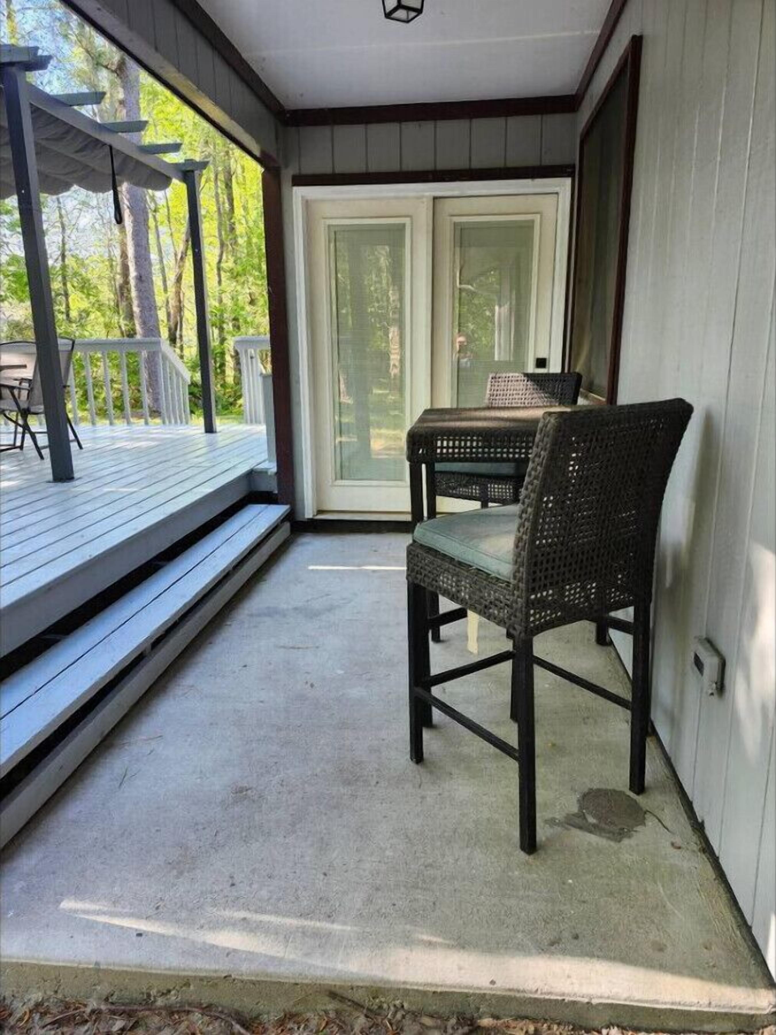 En inglasad veranda med ett bord och stolar, en skjutdörr i glas och utsikt över träd.