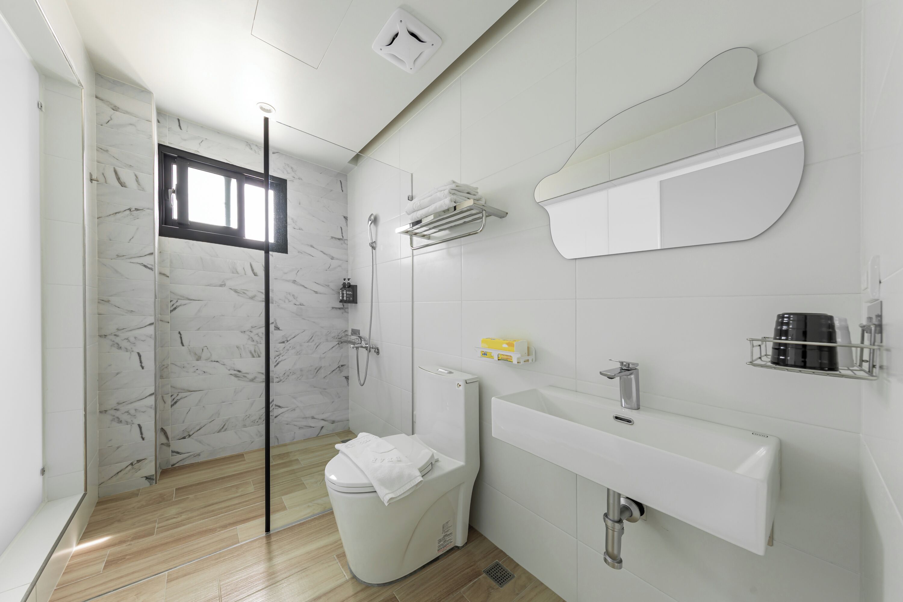 Ein modernes Badezimmer mit einer Duschwand aus Marmor, einer Toilette, einem Waschbecken und einem großen Spiegel.