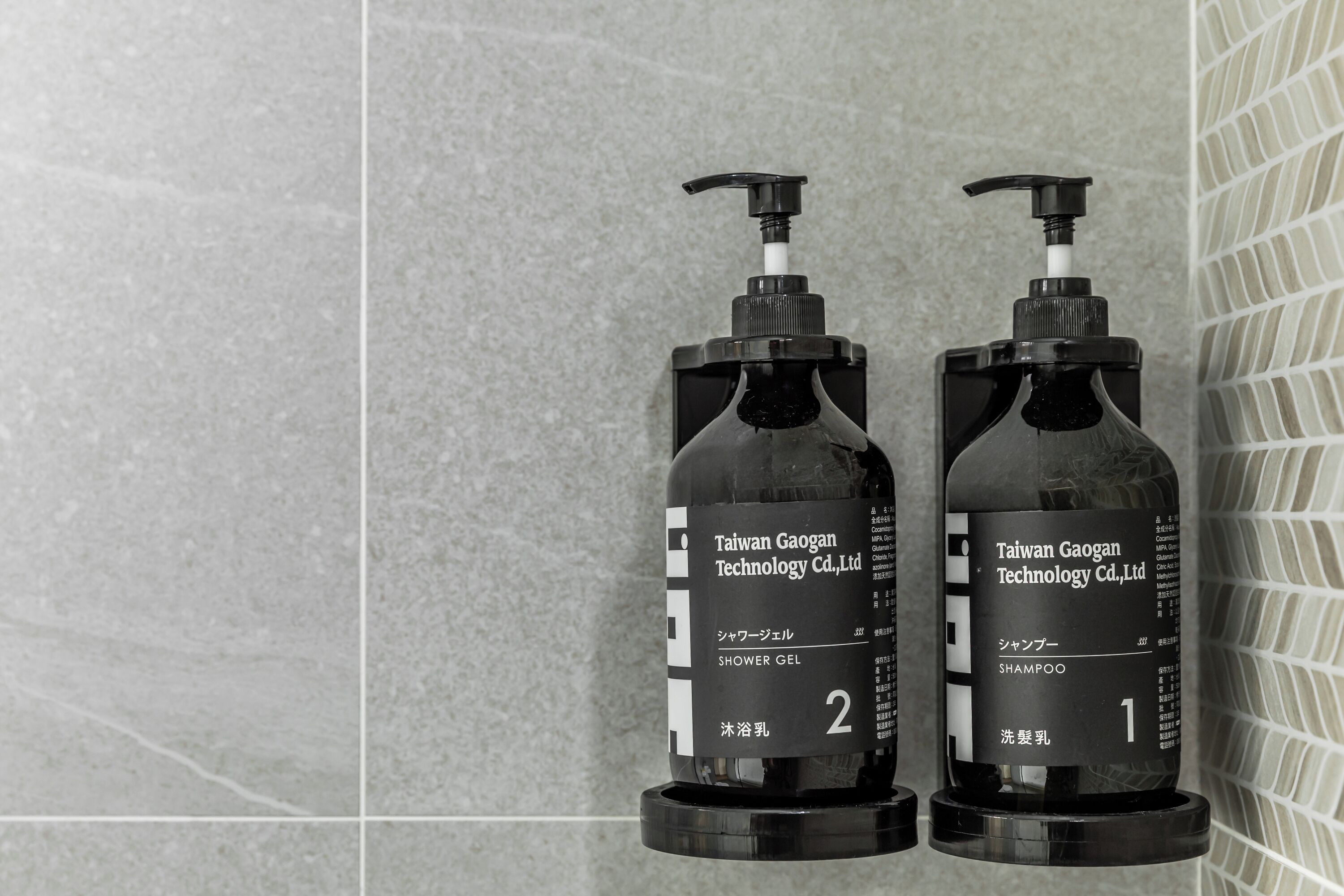 Two black bottles of Taiwan Gaogan Technology Co., Ltd. products, labeled as shower gel and shampoo, on a tiled surface.