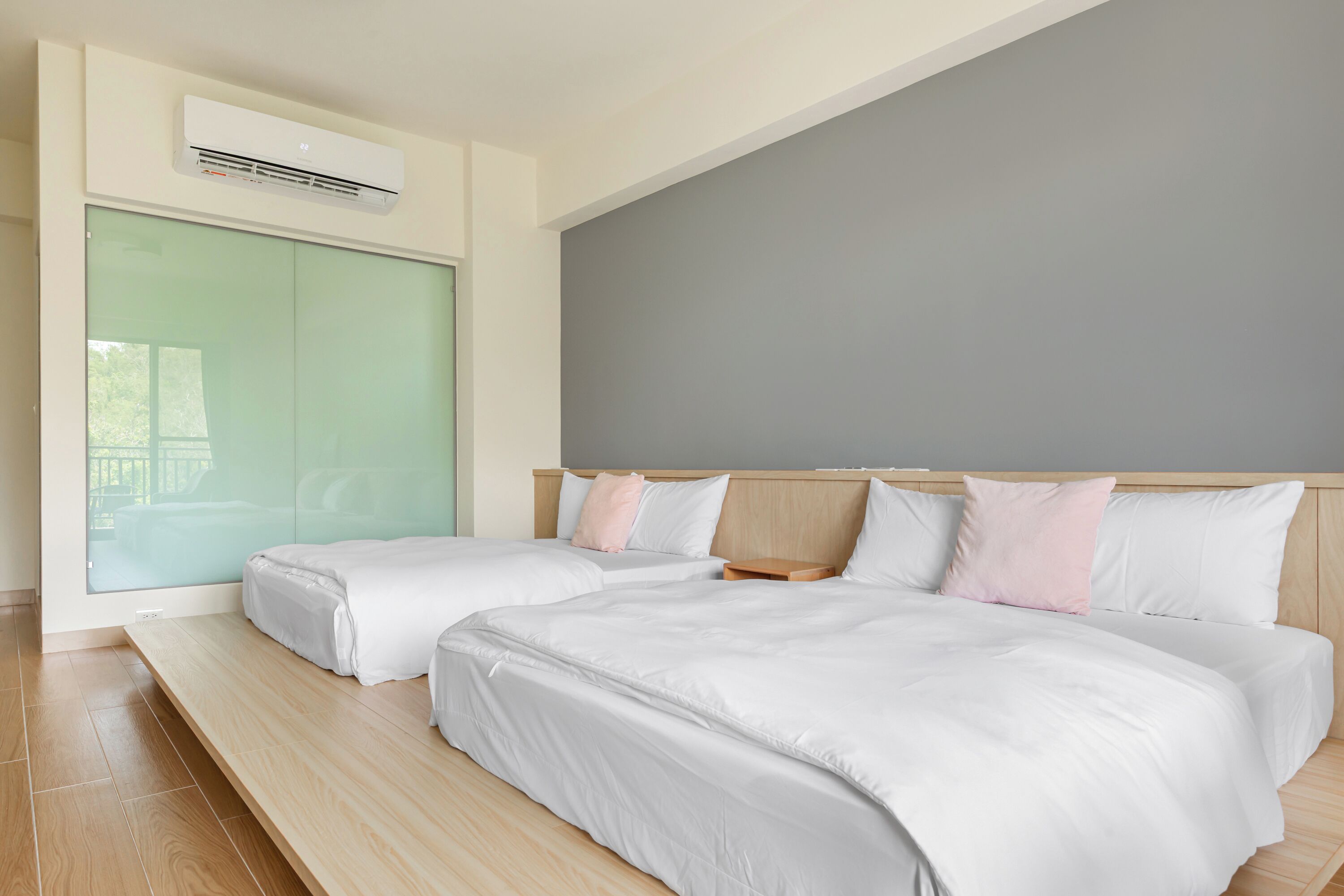 Ein modernes Hotelzimmer mit zwei Betten, einem großen Fenster und einer fest installierten Klimaanlage.