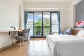 A hotel room with a large bed, a chair, a small table, and a balcony with a view of greenery. - Polar bear bnb  (Liuqiu)
