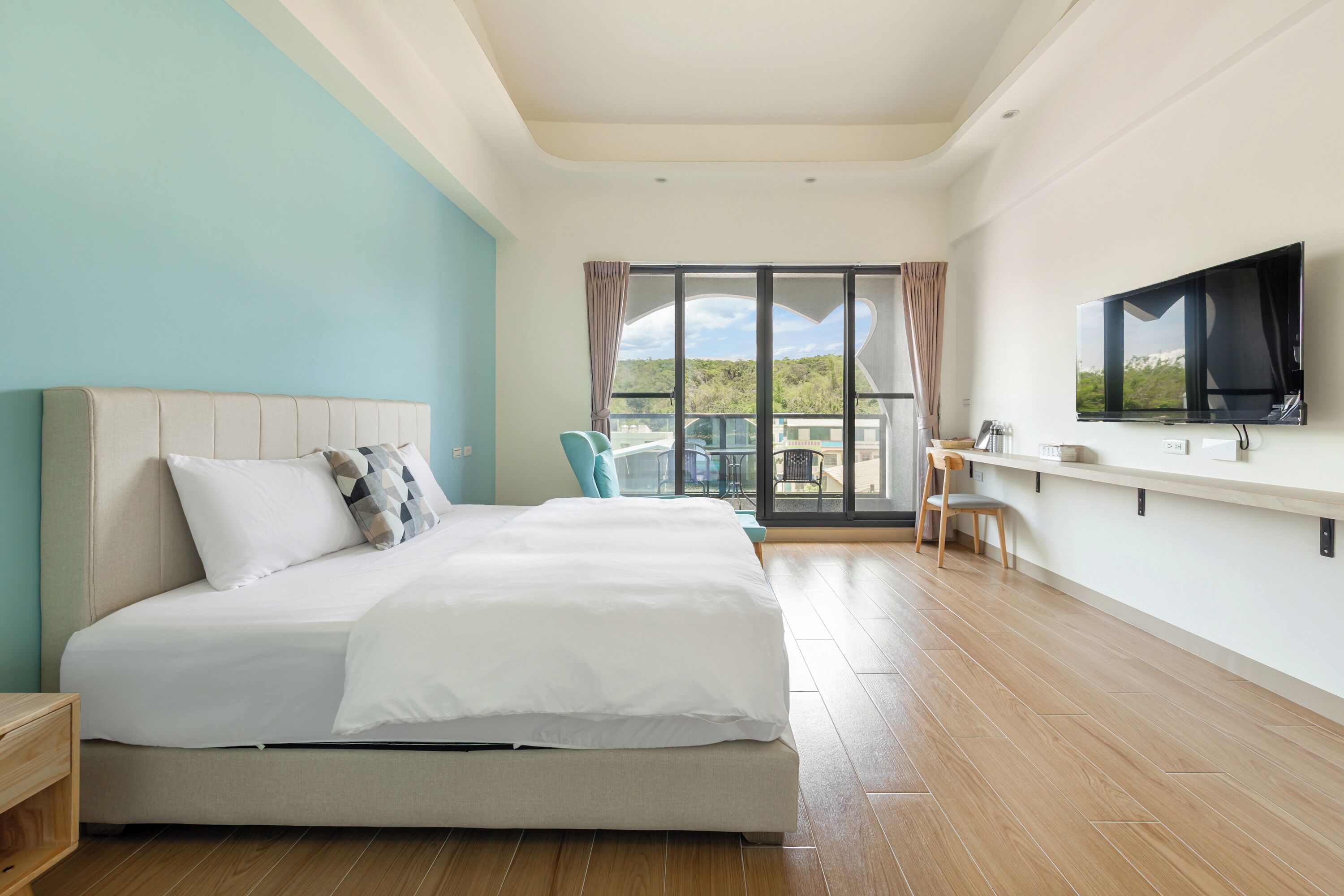 Una habitación de hotel moderna con una cama grande, un televisor, un balcón con vistas y un escritorio con una silla.