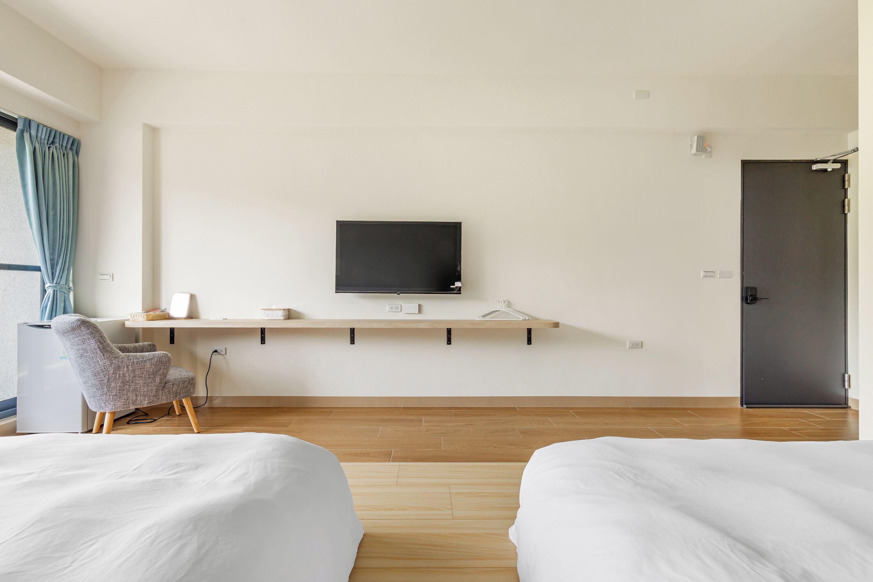 A modern hotel room with a bed, a desk with a flat-screen TV, a chair, and a door.