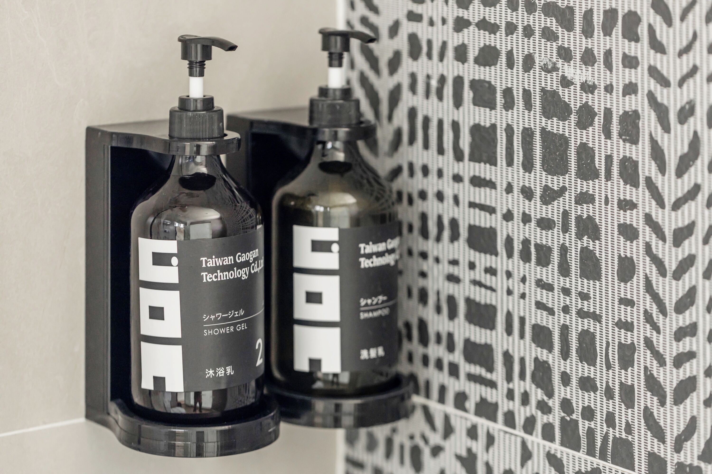 Two bottles of Taiwan Gaogan Technology shower gel on a black shelf against a patterned wall.