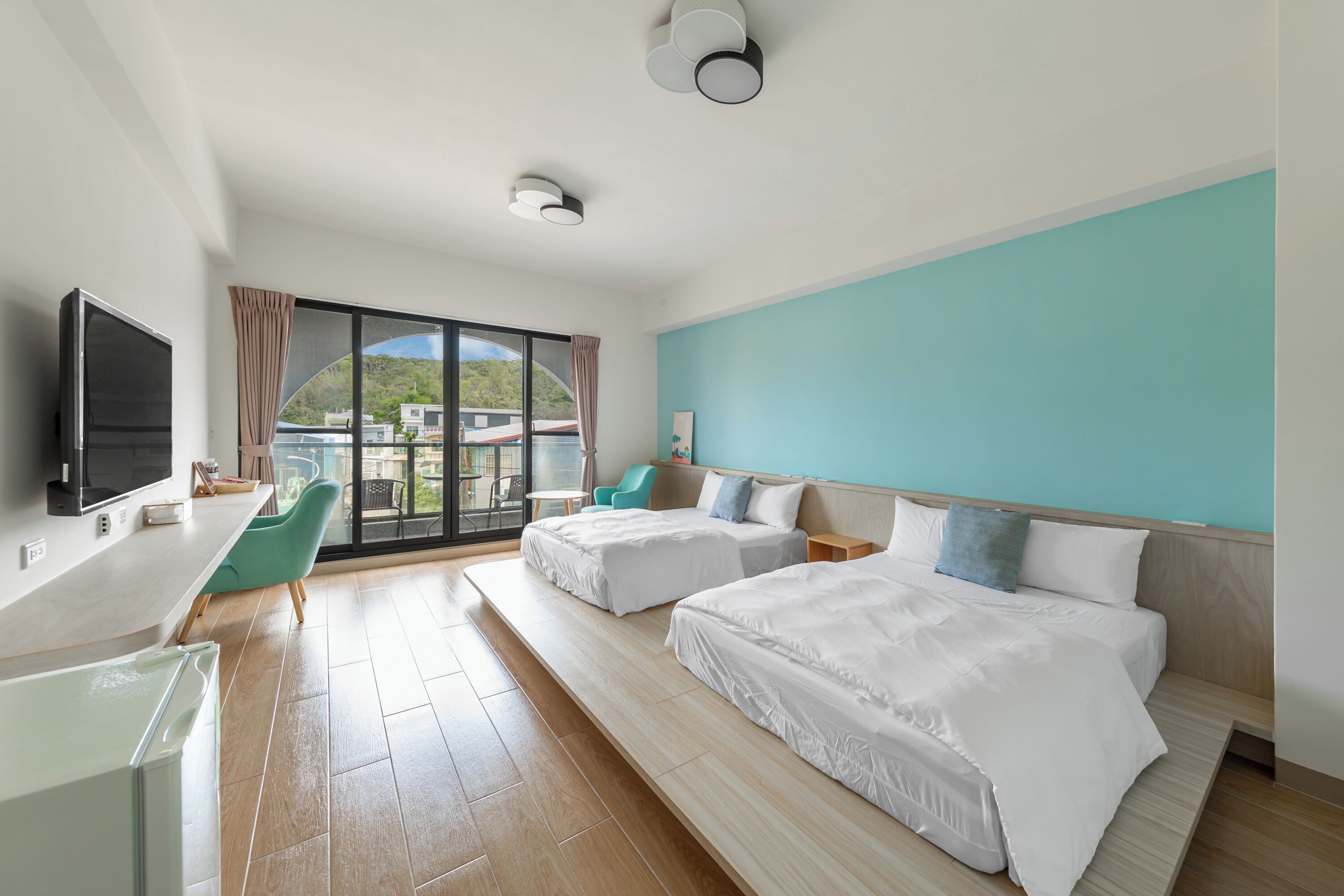Habitación de hotel con dos camas, un escritorio, televisor y vista al exterior.