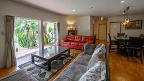 A spacious living room with a red leather sofa, a grey sofa, a glass coffee table, and a dining area with a table and chairs. - Lulu Manza (Onna)