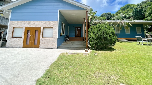 A two-story house with a blue exterior, a stone accent wall, and a covered porch. - Lulu Manza (Onna)