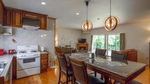A modern kitchen with wooden cabinets, a gas stove, and a dining area with a glass table and chairs. - Lulu Manza (Onna)