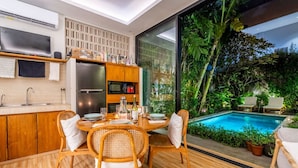 A modern kitchen with a dining area overlooking a pool, featuring wooden furniture and a large window. - Tropical 2BR Villa with Private Pool in Canggu (Kecamatan Kuta Utara)