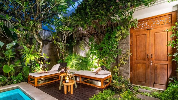A wooden deck with two lounge chairs and a small table, surrounded by lush greenery and a stone wall. - Tropical 2BR Villa with Private Pool in Canggu (Kecamatan Kuta Utara)
