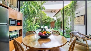A modern kitchen with a dining area, large windows, and a view of a lush garden. - Tropical 2BR Villa with Private Pool in Canggu (Kecamatan Kuta Utara)