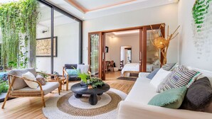 A modern living room with a large window, a black coffee table, a white sofa, and a dining area with a wooden table and chairs. - Tropical 2BR Villa with Private Pool in Canggu (Kecamatan Kuta Utara)