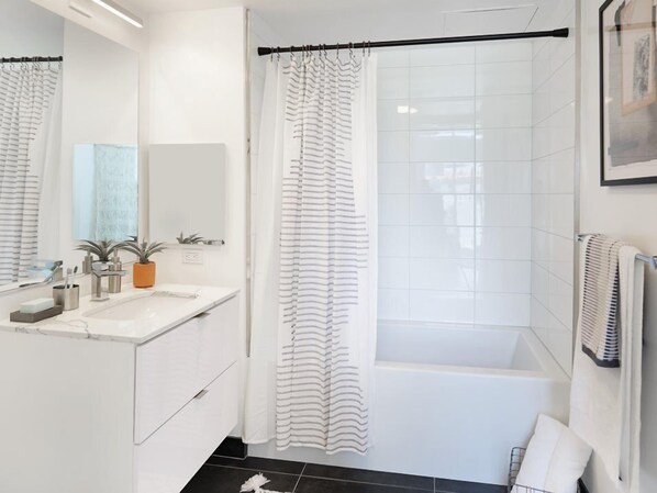 A modern bathroom with a white vanity, a bathtub, and a shower curtain.