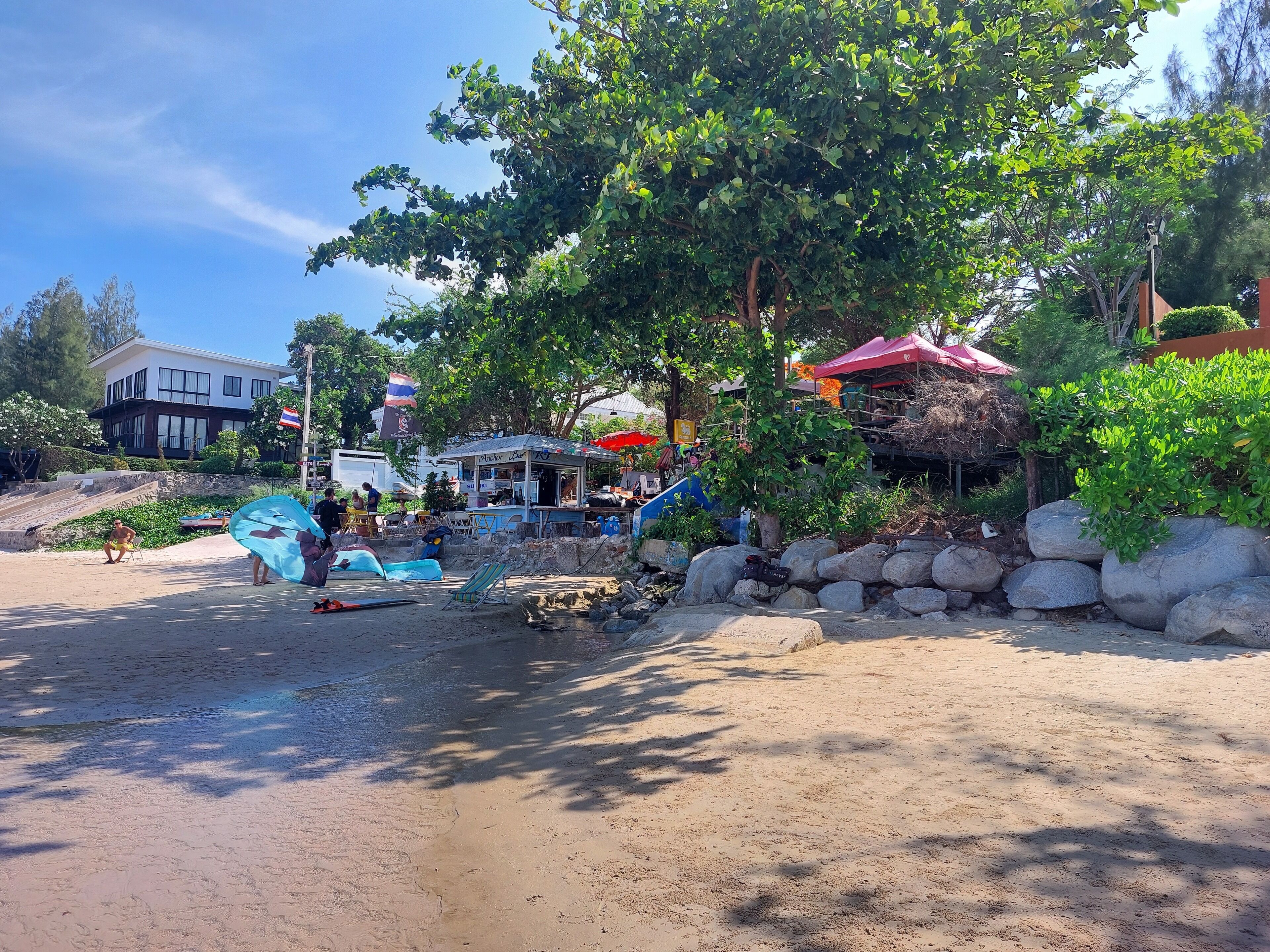 A beachside café with outdoor seating, a small kiosk, and a stone wall.
