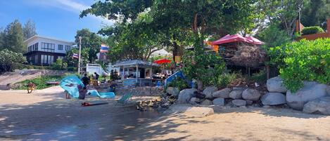 A beachside café with outdoor seating, a small kiosk, and a stone wall.