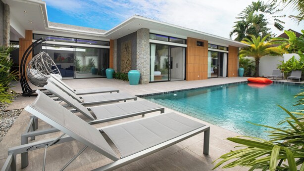 A modern house with a swimming pool, lounge chairs, and a hanging chair.