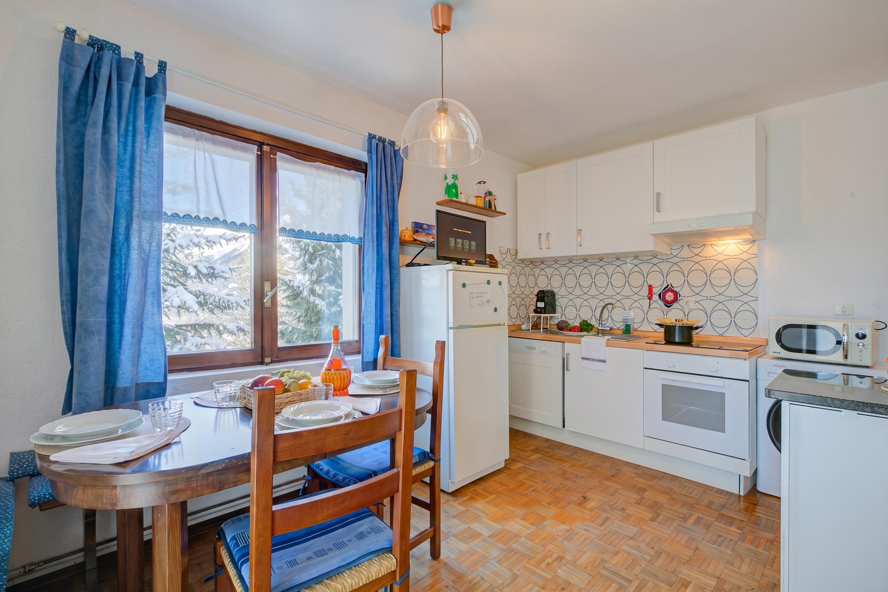 A compact kitchen with white cabinets, a dining table with chairs, a refrigerator, a microwave, and a sink.