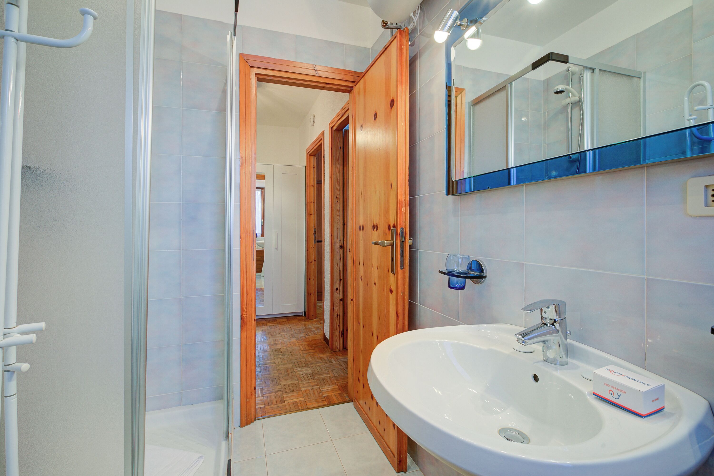 A bathroom with a wooden door, a white sink, and a mirror above it.