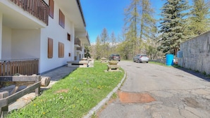 A street view with a building on the left, a sidewalk with grass, and cars parked on the right.