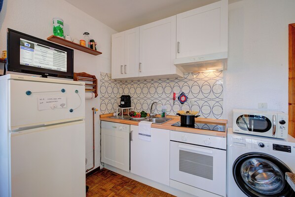 A compact kitchen with a refrigerator, microwave, oven, and washing machine.