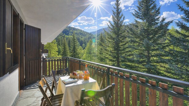 A balcony with a table set for two, overlooking a forested mountain area.