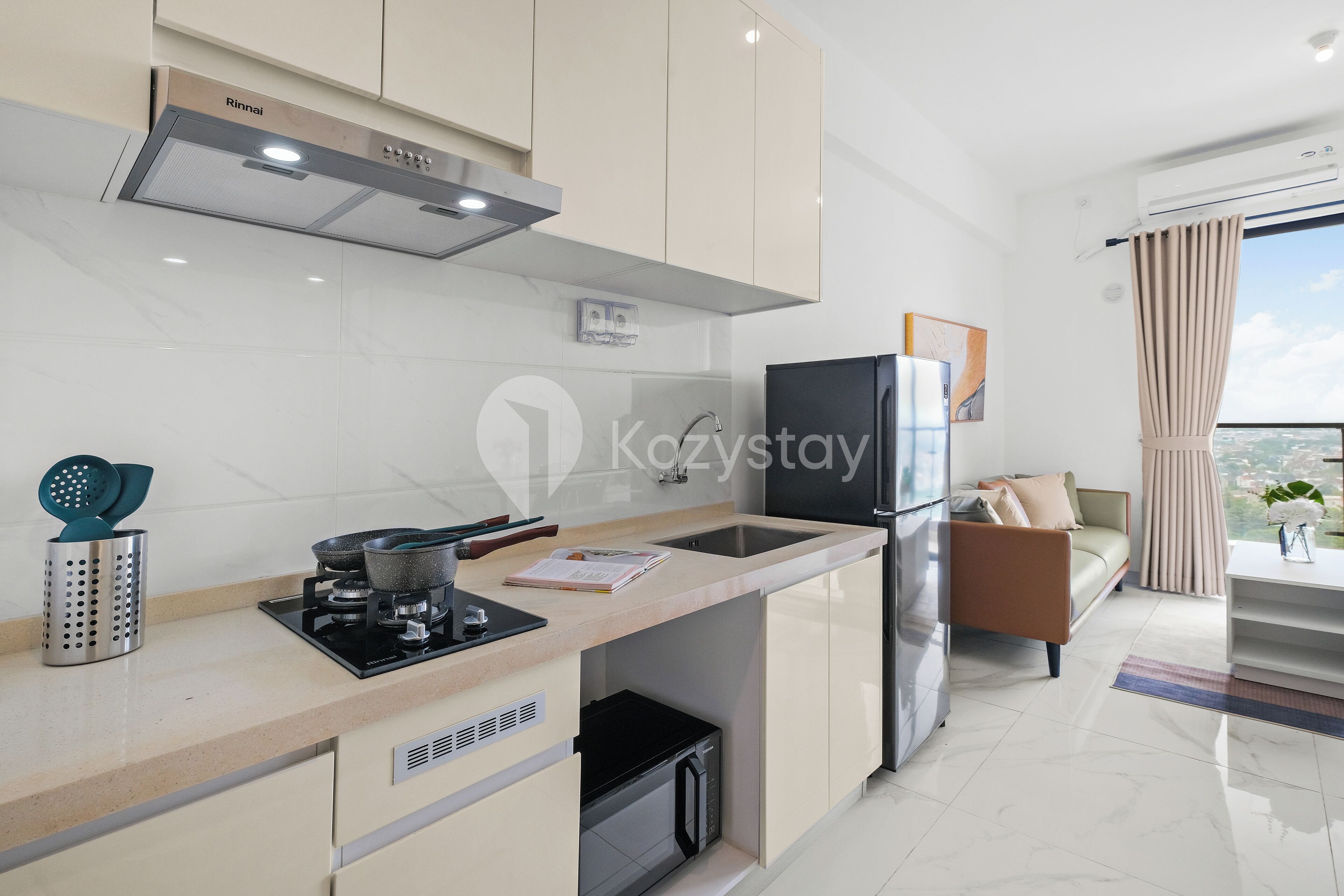 Eine moderne Küche mit Einbauherd, Spüle und Kühlschrank. Ein Essbereich mit Sofa und einem fensterbepflanzten Fenster.