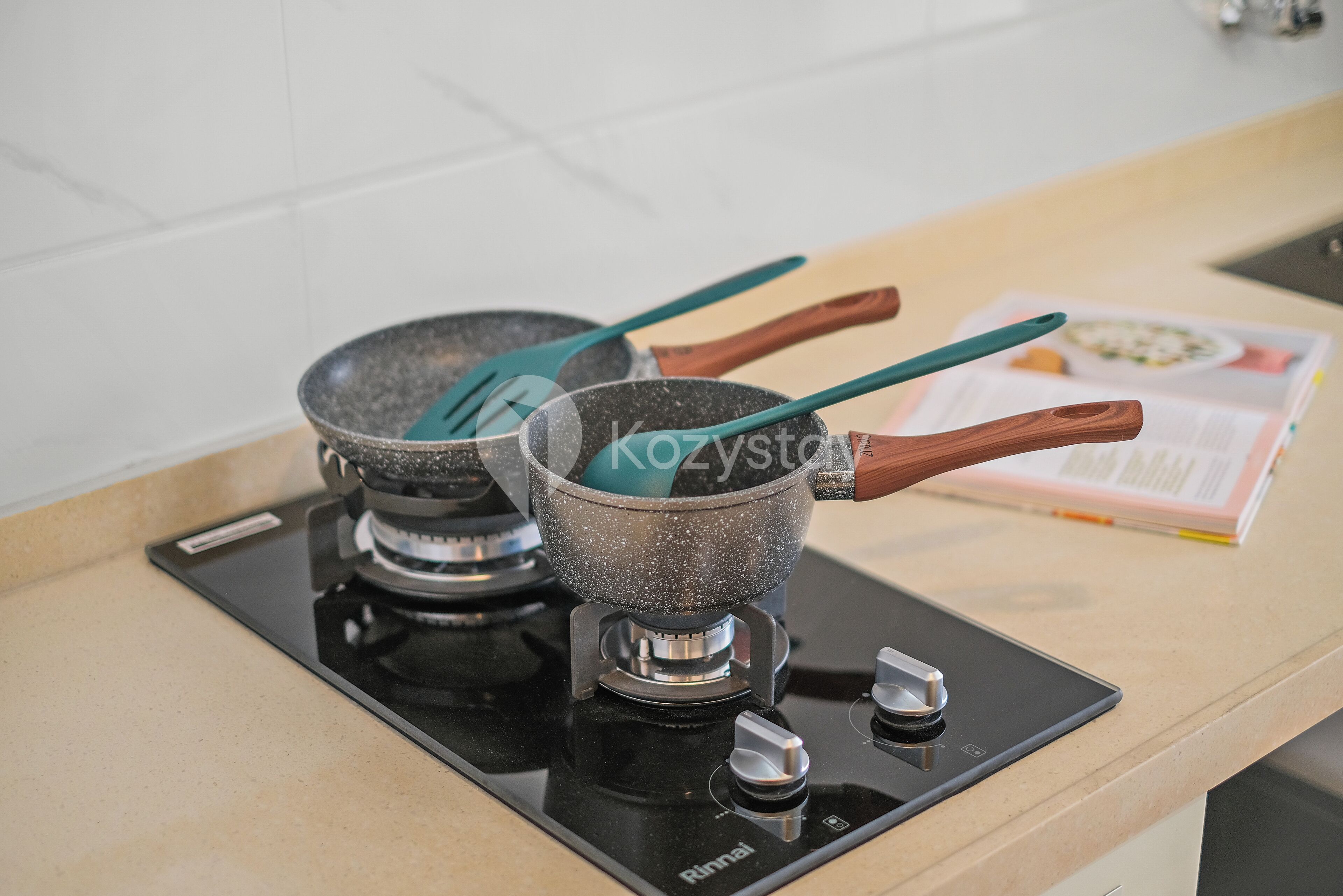 A kitchen with a black induction cooktop, two pots with wooden handles, and a cookbook on the counter.