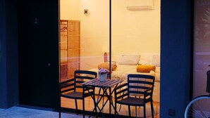 Un interior moderno con un vidrio que da a una zona de estar acogedora, con un sofá, cojines y una pequeña mesa con sillas.