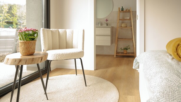 Un dormitorio moderno con un ventanal grande, una mesa redonda de madera con una planta en maceta, un sillón mullido, una cama con almohada amarilla y una estantería de escalera de madera.