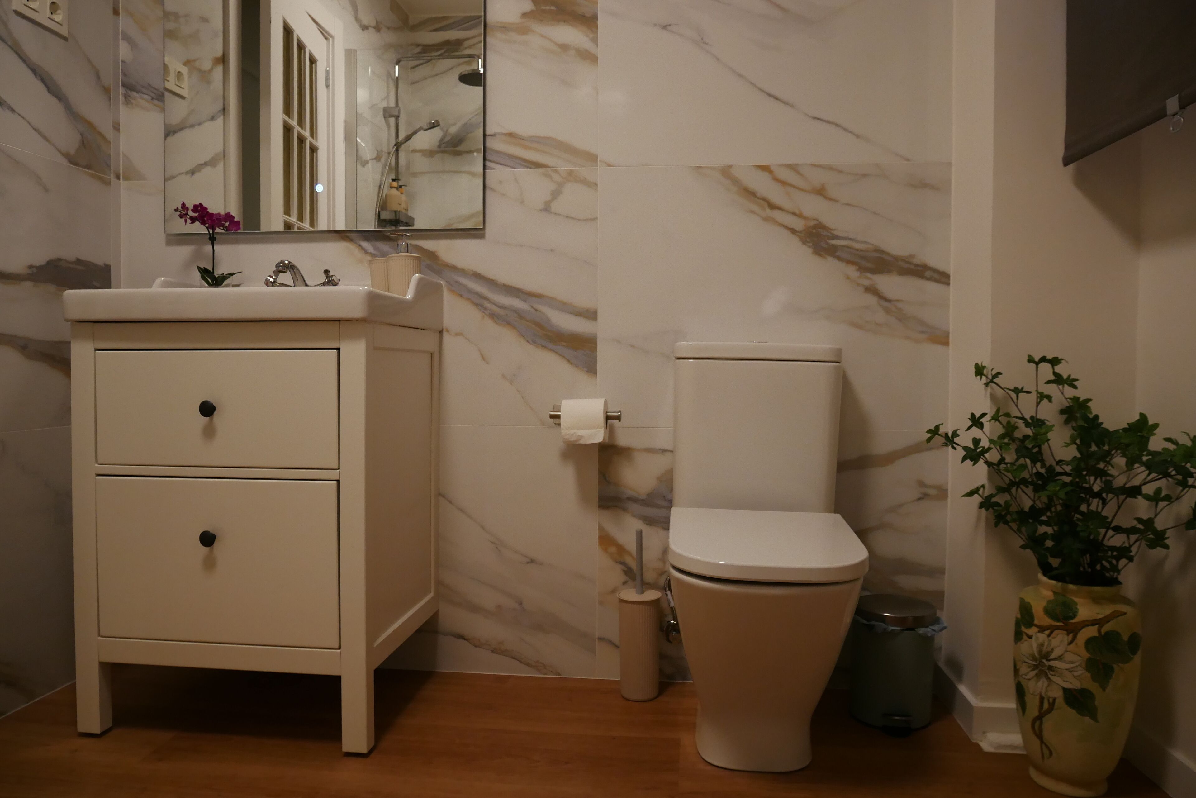 Une salle de bain avec un mur en marbre, des toilettes, un lavabo avec un miroir et une poubelle.