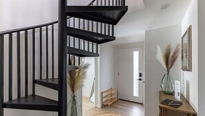 Un intérieur moderne avec un escalier en colimaçon noir, une console en bois et un tapis tissé.