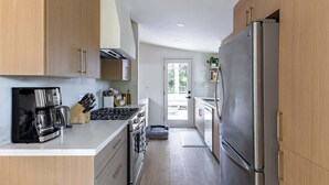 Une cuisine moderne avec des meubles en bois clair, des appareils électroménagers en acier inoxydable et un îlot central.