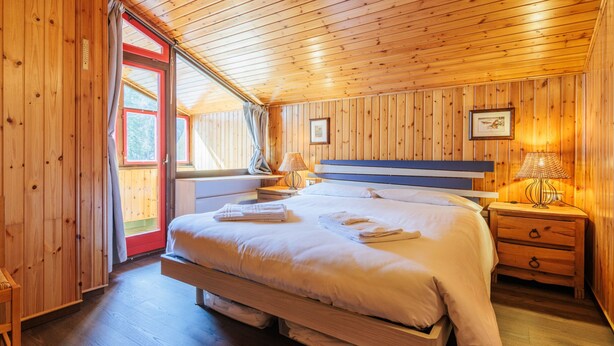 A wooden cabin bedroom with a large bed, bedside tables, a window with curtains, and a wooden ceiling. - Boiserie by Interhome (Campitello)