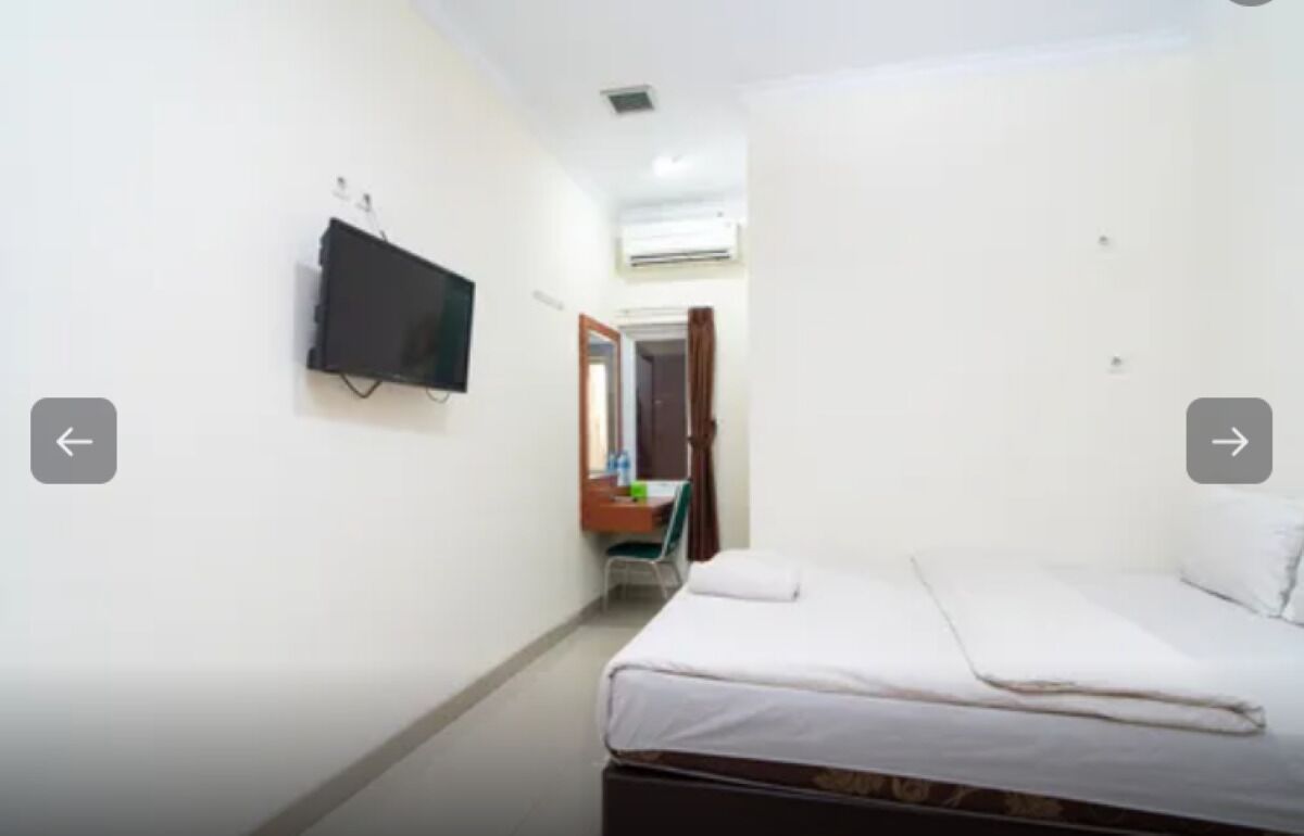 Una habitación pequeña y limpia con una cama, un televisor montado en la pared y un espejo sobre un escritorio.