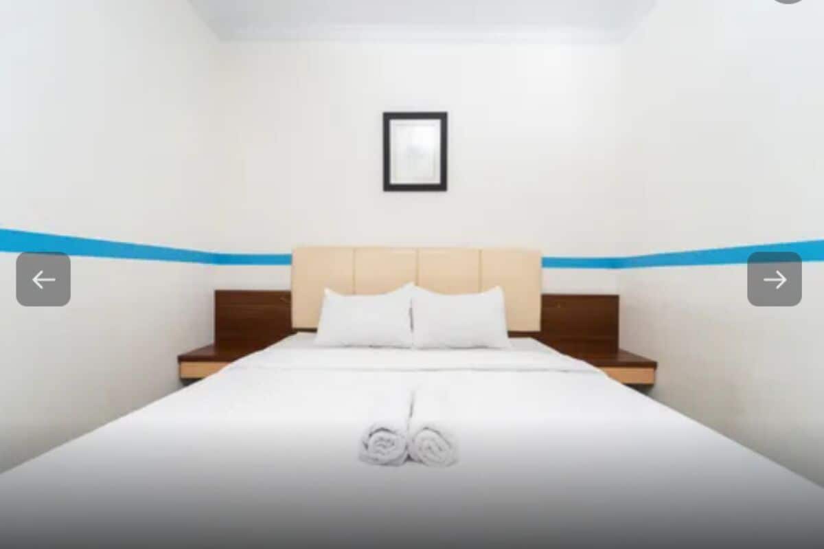A neatly made bed with white linens and a folded towel at the foot.