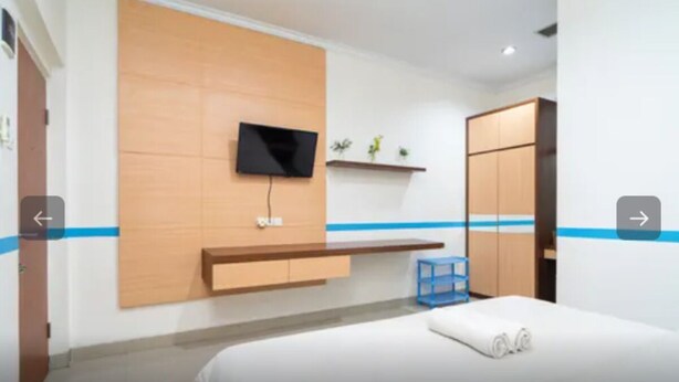 A modern hotel room with a bed, a mounted TV, a wooden panel wall, a blue accent wall, and a wardrobe. - Tebet Utara Residence (Jakarta)