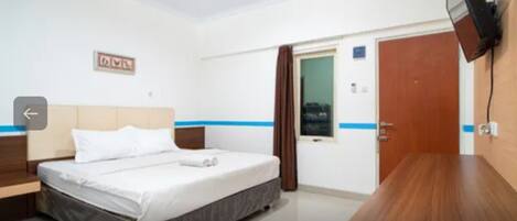 A hotel room with a bed, a wooden nightstand, a flat-screen TV mounted on the wall, and a door with a window.