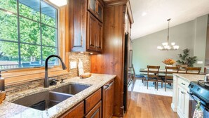 Una cocina con gabinetes de madera, encimeras de granito, un lavamanos doble y un comedor con candelabro.