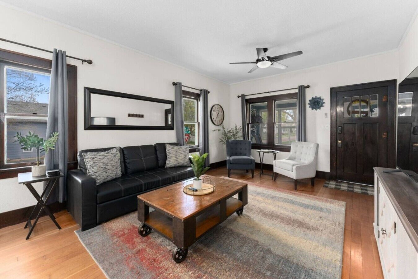 A living room with a sofa, a coffee table, a chair, a ceiling fan, and a door.