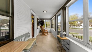 En overdækket veranda med en træbænk, en gyngestol og et metalbord med en vandkande.