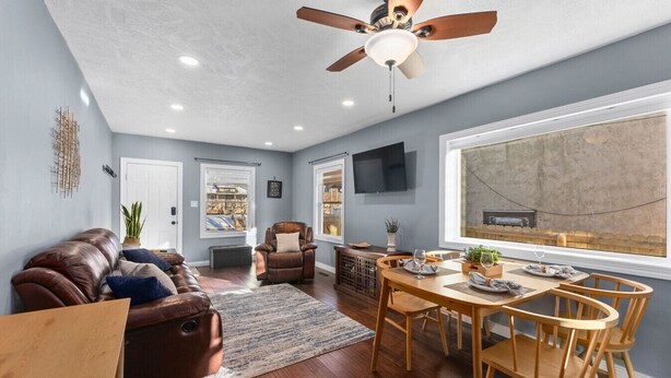 A spacious living room with a brown leather couch, a dining area with wooden chairs and a table, and a ceiling fan.
